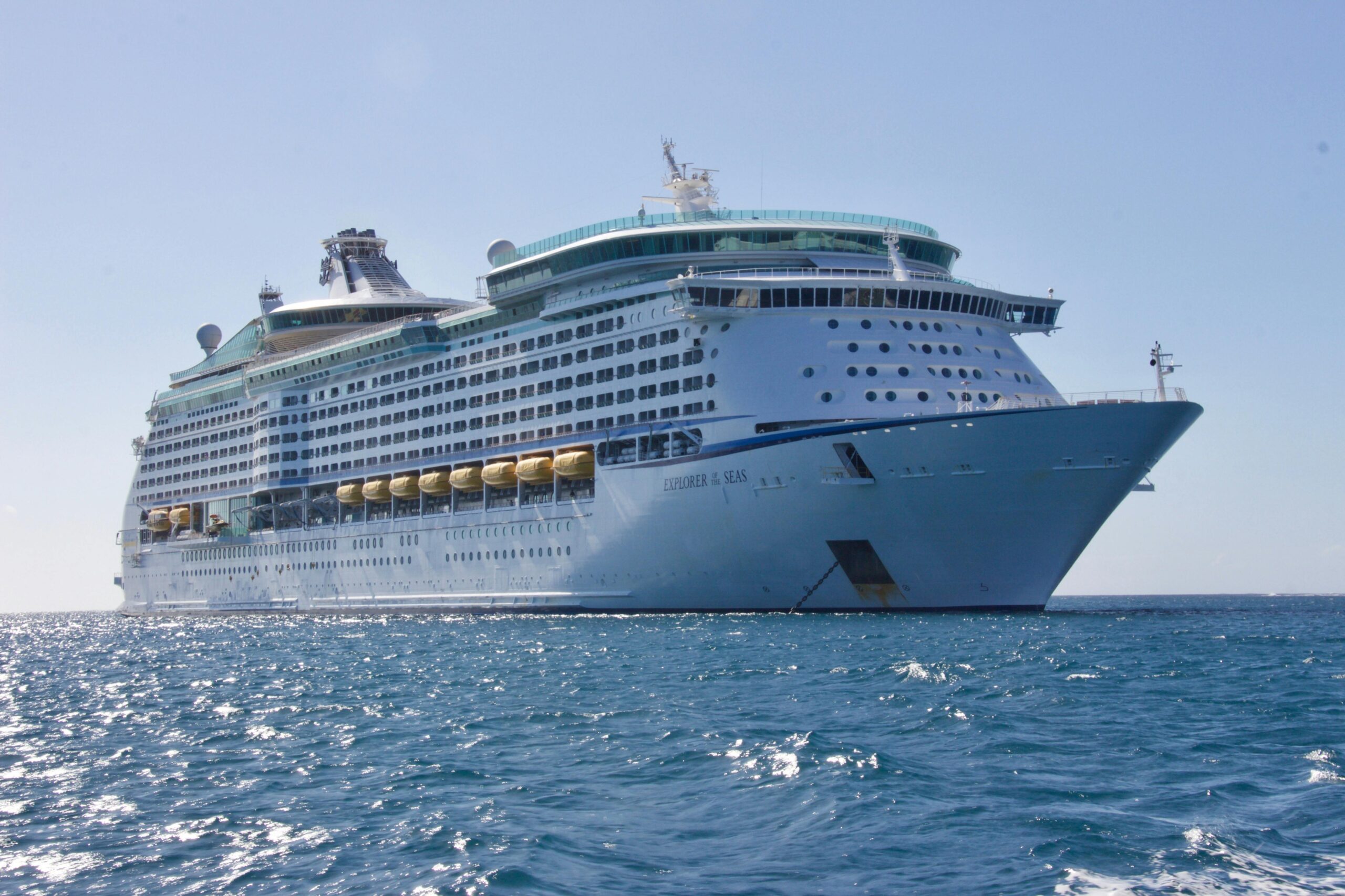 A large white Singer Group cruise ship sails on calm blue water under a clear sky, with multiple decks and rows of balcony cabins visible.